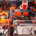 Detailed view of a 3D printer with filament and tools in a workshop setting.